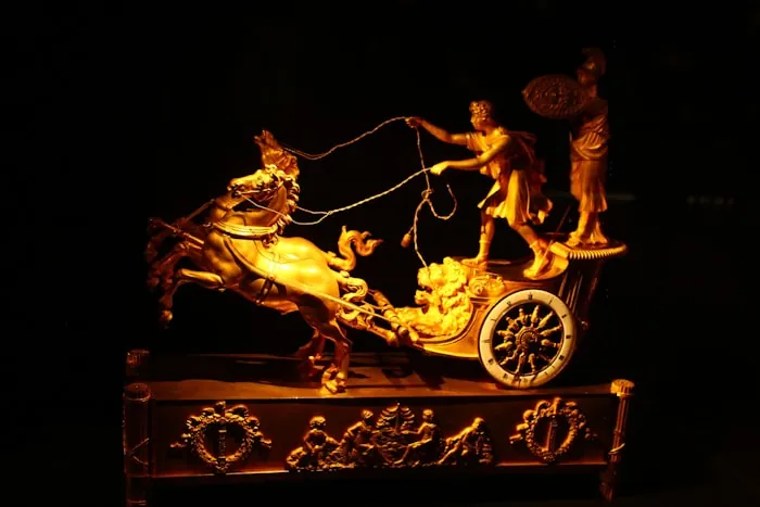 Gilded chariot and horses sculpture lit against a dark background